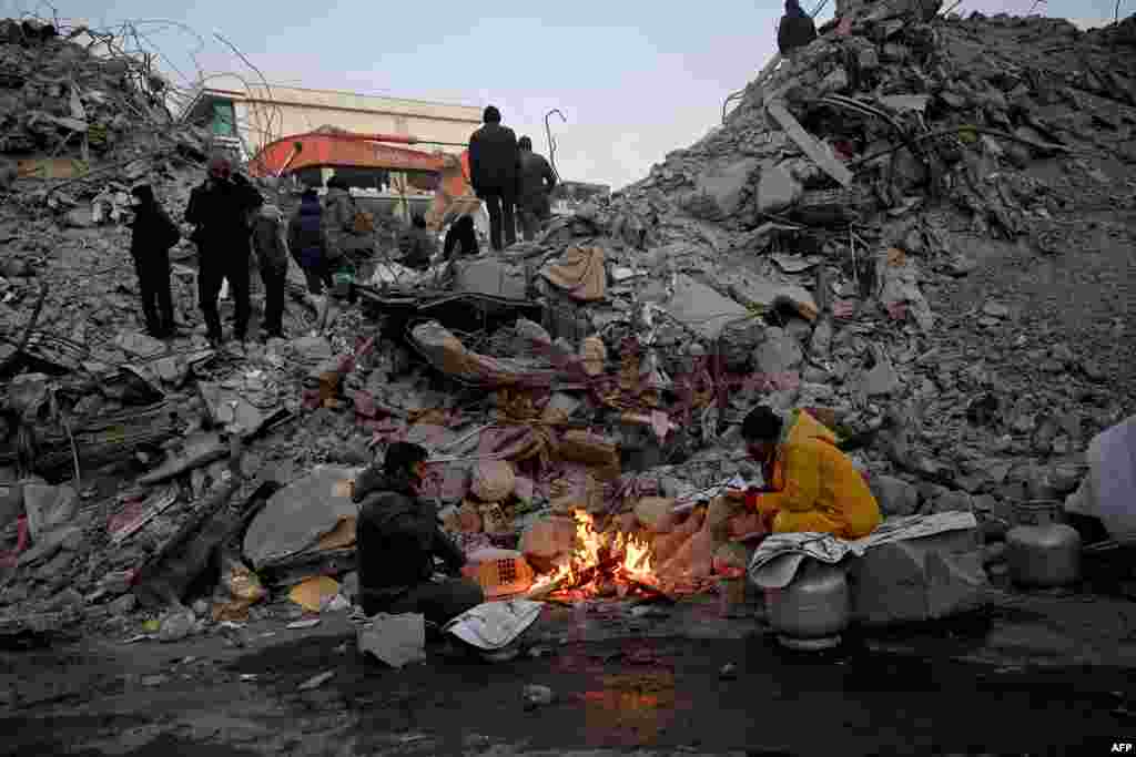 People warm up around a fire in front of rubble of collapsed buildings as rescue teams continue to search victims and survivors, after a 7.8 magnitude earthquake struck in Kahramanmaras, Turkey.