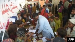 FILE - Families displaced by floods gather around a paramedic at a makeshift medical camp set in Dadu district, Sindh province in Pakistan on Sept. 27, 2022.