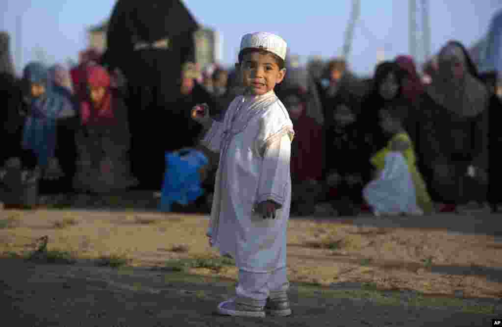 Seorang anak Palestina mengenakan pakaian traditional berdiri depan para perempuan yang sedang melaksanakan salat ied, di Timur Kota Gaza, Jumat, 15 Juni 2018. (Foto: AP)