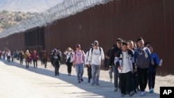 A group of people, including many from China, walk along the wall after crossing the border with Mexico to seek asylum, Tuesday, Oct. 24, 2023, near Jacumba, California. (AP Photo/Gregory Bull)