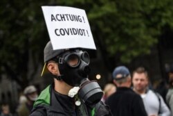 A man with a placard reading in German: 'Watch out! Covidiot' takes part in a protest against the increasing coronavirus preventative measures in Zurich, Switzerland, Aug. 29, 2020.