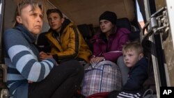 A mother, left, sits in the back of a bus with her children in the town of Bashtanka, after they fled from Snihurivka village, in Ukraine's Mykolaiv region, April 7, 2022, as Russia continues its invasion of Ukraine.