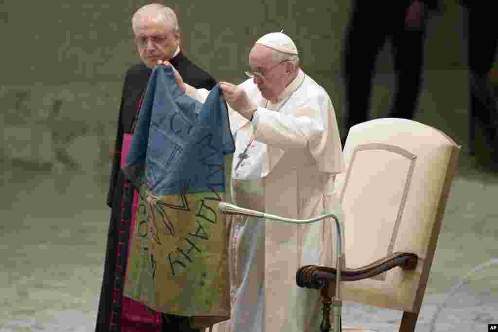 Pope Francis shows a flag that he said was brought to him from Bucha, Ukraine, during his weekly general audience in the Paul VI Hall, at the Vatican.