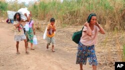 FILE - Displaced people from Myanmar carry donated lunch boxes to their tents along the Thai side of the Moei River in Mae Sot, Thailand on Feb. 5, 2022.