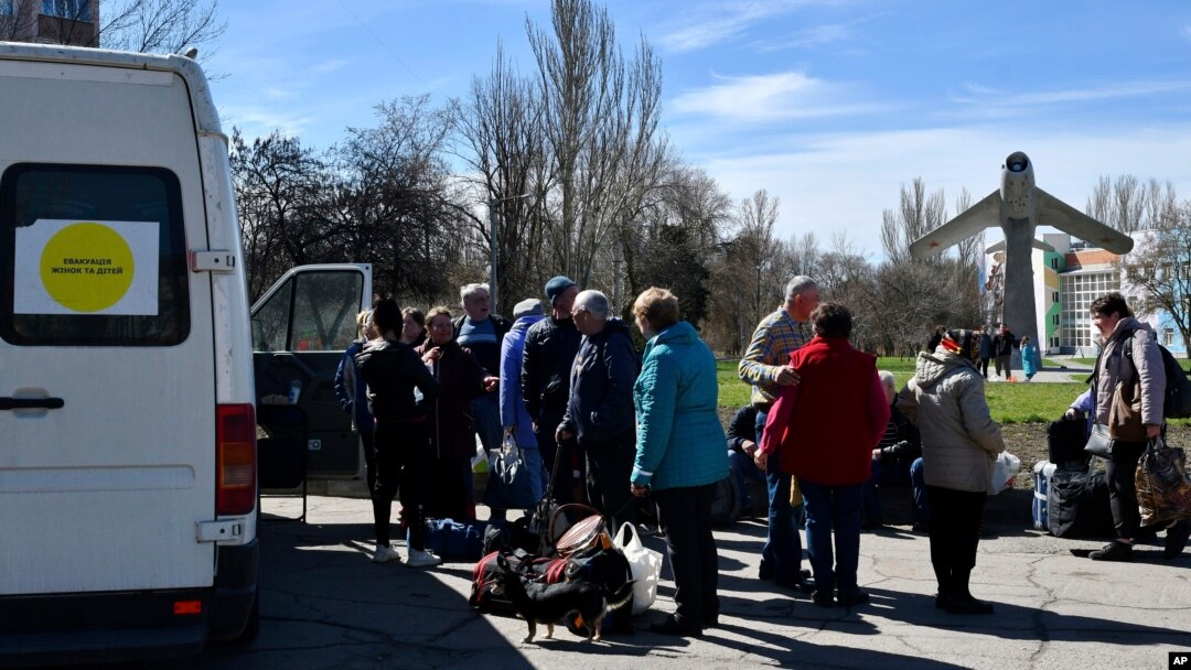 People wait to board a bus during their evacuation, with a MiG-17 fighter jet monument in the background, in Kramatorsk, Ukraine, April 9, 2022.
