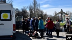 People wait to board a bus during their evacuation, with a MiG-17 fighter jet monument in the background, in Kramatorsk, Ukraine, April 9, 2022.