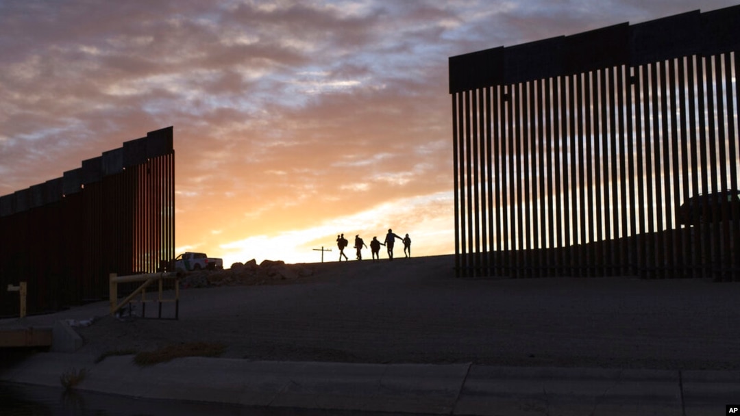 FILE - A pair of migrant families from Brazil pass through a gap in the border wall to reach the United States after crossing from Mexico to Yuma, Ariz., to seek asylum, June 10, 2021.