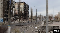 2022年4月6日，在基辅郊区城镇博罗江卡，少数居民骑着自行车经过被摧毁的楼群。(美国之音希瑟·默多克拍摄)