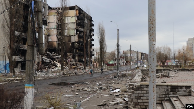 2022年4月6日，在基輔郊區城鎮博羅江斯克，少數居民騎著自行車經過被摧毀的樓群。 (美國之音希瑟·默多克拍攝)