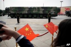 FILE - Spectators wave Chinese flags as military vehicles carrying DF-41 ballistic missiles roll during a parade to commemorate the 70th anniversary of the founding of Communist China in Beijing, Oct. 1, 2019.