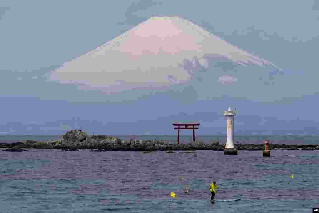 With Mount Fuji in the background, a standup paddleboarder cruises near a Torii gate, an entrance gate to a Shinto shrine, in Sagami Bay, in Zushi, south of Tokyo, Japan.