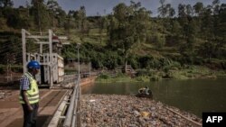 Petugas pembangkit listrik tenaga air Ruzizi 1, mengamati rekannya di atas sampan tengah memeriksa tingkat sampah plastik Sungai Ruzizi di sekitar bendungan di Bukavu, Republik Demokratik Kongo timur, 16 Maret 2022. (Guerchom NDEBO/AFP). 