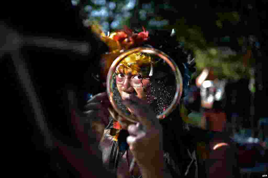 A woman of the Truka tribe looks at herself in the mirror on the fourth day of the Terra Livre Indigenous Camp in Brasilia, Brazil on April 7, 2022. (Photo by CARL DE SOUZA / AFP)