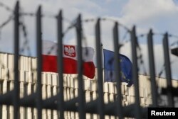 FILE - A view through a fence shows flags of Poland and European Union outside the Polish embassy in Moscow, Russia, March 29, 2018.