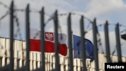 FILE - A view through a fence shows flags of Poland and European Union outside the Polish embassy in Moscow, Russia, March 29, 2018. 