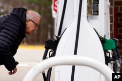 FILE - A man checks gas prices at a gas station in Buffalo Grove, Ill., March 26, 2022. Since Russia's invasion of Ukraine began on February 24, prices for fuel and food have jumped.