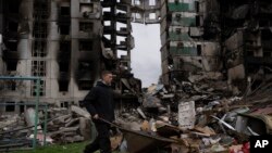 A young man pushes a wheelbarrow in front of a destroyed apartment building in the town of Borodyanka, Ukraine, April 10, 2022. 