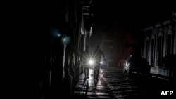 A car's headlights are seen past people walking on a dark street in San Juan, Puerto Rico, after a major power outage hit the island, April 6, 2022.