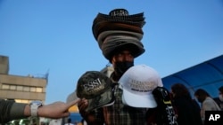 A man sells hats with the name of Mexican singer Alejandro Fernandez and Colombian singer Jessi Uribe as people line up to get into the concert in Caracas, Venezuela, March 3, 2022. (AP Photo/Ariana Cubillos, File)