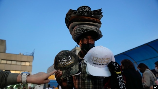 A man sells hats with the name of Mexican singer Alejandro Fernandez and Colombian singer Jessi Uribe as people line up to get into the concert in Caracas, Venezuela, March 3, 2022. (AP Photo/Ariana Cubillos, File)