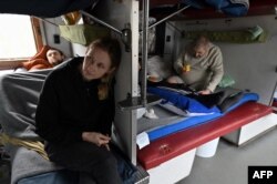 Yulia Perepelytsia (C), 29, sits on the bed of her husband Evhen (L), 30, a patient on a medical evacuation train on its way to the western Ukrainian city of Lviv, April 10, 2022.