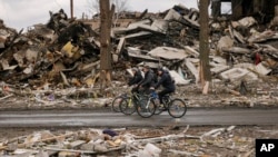 Sejumlah pria tampak mengayuh sepeda melewati gedung-gedung apartemen yang hancur di Borodyanka, Ukraina, pada 6 April 2022. (Foto: AP/Vadim Ghirda)