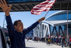 Hailun Song waves a U.S. flag and cheers marchers as a "Stop Asian hate" rally in downtown Atlanta passes by, March 20, 2021.