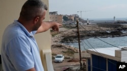 Seorang pria Lebanon menunjuk ke arah pantai di Batroun, di utara Lebanon di mana para pejabat Lebanon mengatakan sekelompok pria bersenjata mendarat dan membawa seorang kapten kapal, Sabtu, 2 November 2024. (Foto: Hussein Malla/AP Photo)