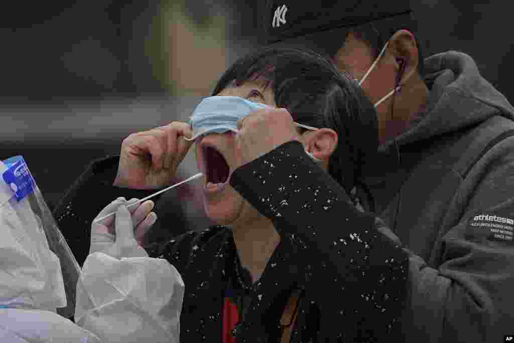 A woman pulls up her mask to get a swab at a coronavirus testing site near residential buildings in Beijing, China.