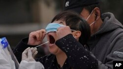 বেইজিংয়ের একটি করোনাভাইরাস পরীক্ষাকেন্দ্রে মাস্ক সরিয়ে এক নারী তার নিয়মিত কোভিড-১৯ পরীক্ষার জন্য নমুনা দিতে প্রস্তুত হচ্ছেন, ৭ ডিসেম্বর 