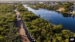 FILE - Texas Department of Safety vehicles line up on the Texas side of the Rio Grande with Mexico visible, right, near an encampment of migrants, Sept. 22, 2021, in Del Rio, Texas.