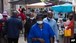 FILE - A woman wearing a mask to protect against the coronavirus walks through the busy Bara Taxi Rank in Soweto, South Africa, April 5, 2022.