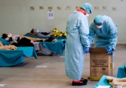 Paramedics carry an hazardous medical waste box as patients lie on camping beds, in one of the emergency structures that were set up to ease procedures at the Brescia hospital, northern Italy, March 12, 2020.
