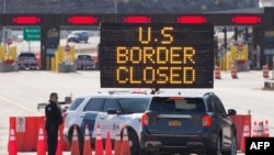 FILE - US Customs officers speaks with people in a car beside a sign saying that the US border is closed at the US/Canada border in Lansdowne, Ontario, on March 22, 2020.
