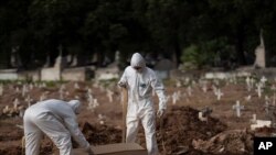 FILE - Cemetery workers in protective clothing maneuver the coffin of 57-year-old Paulo Jose da Silva, who died from the new coronavirus, in Rio de Janeiro, Brazil, June 5, 2020. 
