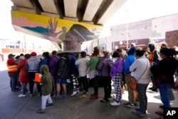 FILE - People surround a car as it arrives carrying food donations at a makeshift camp for migrants seeking asylum in the United States at the border crossing in Tijuana, Mexico, March 12, 2021.