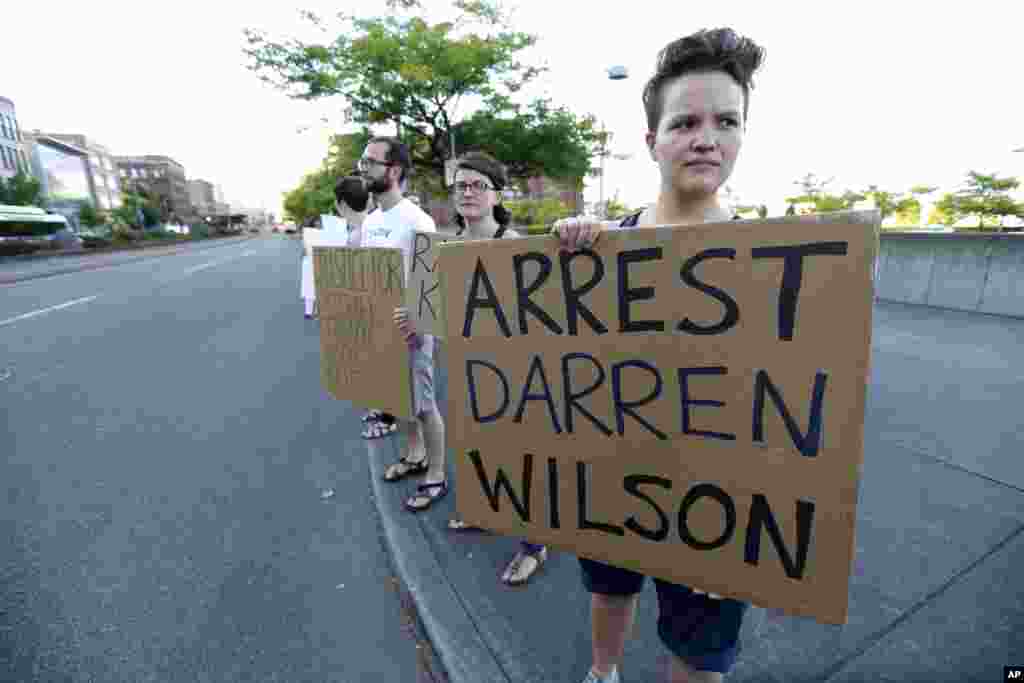 Protester Hana Kato holds a sign naming the police officer that shot the teenager as she attends an evening rally, Tacoma, Washington, Aug. 19, 2014.