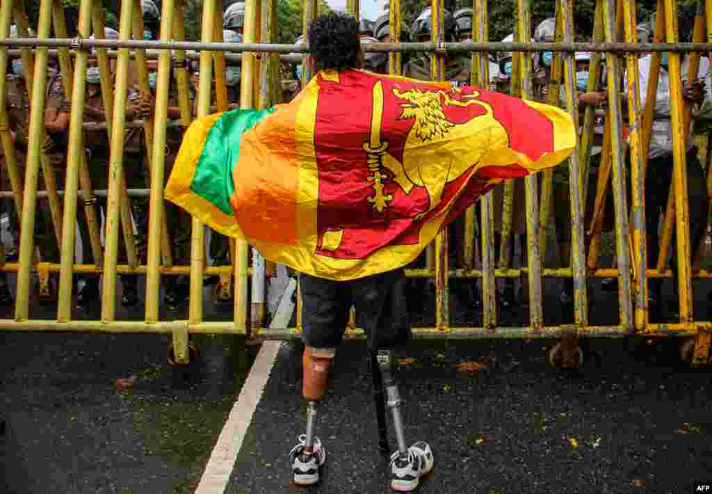 A retired soldier carrying a Sri Lanka national flag stands next to a police barrier during a demonstration against the economic crisis near the parliament building in Colombo. (Photo by AFP)