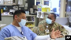 In this image provided by the U.S. Army, U.S. Air Force Tech Sgt. Deundre Bryant, right, a medical administrator, checks up on Tech Sgt. Rony Castaneda-Zamora a medical technician, while supporting the COVID response operations at University of Rochester 