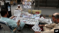 People read copies of morning newspapers carrying headline news of the Supreme Court decision against Prime Minister Imran Khan's ruling, at a stall, in Peshawar, Pakistan, April 8, 2022. 