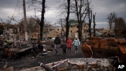 A family walks amid destroyed Russian tanks in Bucha, on the outskirts of Kyiv, Ukraine, April 6, 2022.