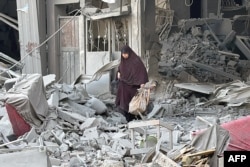 TOPSHOT - Seorang perempuan berjalan di atas reruntuhan bangunan menyusul serangan Israel di Beit Lahia di Jalur Gaza utara, 28 Oktober 2024. (AFP)