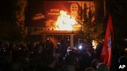 Fire burns behind a riot police cordon and in front of a poster depicting the Albania Prime minister Edi Rama during an anti-government rally set up by the opposition, in Tirana, Albania, Monday, Oct. 7, 2024. 