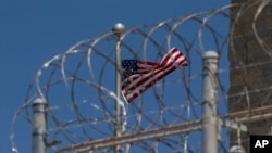 FILE - In this April 17, 2019, photo reviewed by U.S. military officials, a U.S. flag flies behind a razor wire fence of the Camp VI detention facility at Guantanamo Bay Naval Base, Cuba. 