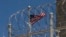 FILE - In this April 17, 2019 file photo reviewed by U.S. military officials, a U.S. flag flies behind razor wires of the Camp VI detention facility at Guantanamo Bay Naval Base, Cuba. 