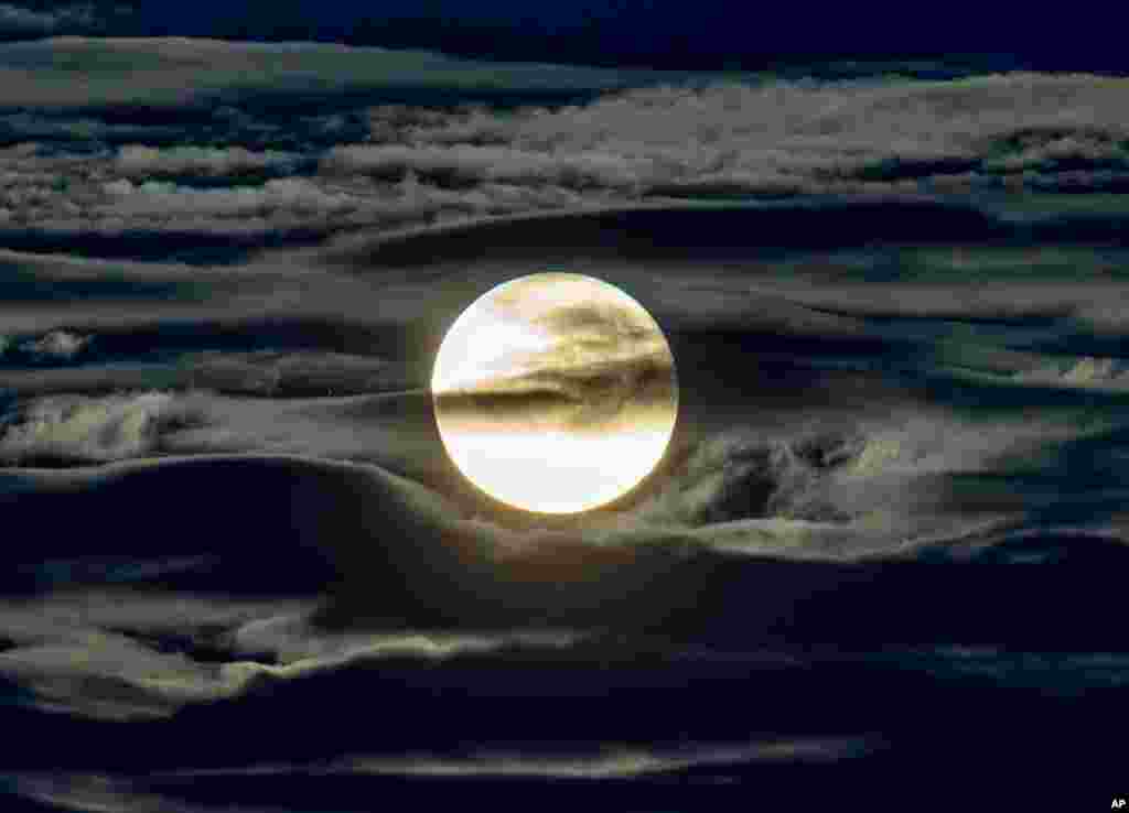 The full moon shines through as it is surrounded by clouds, as seen from the outskirts of Frankfurt, Germany.