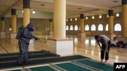 Seorang pria sedang salat saat petugas menyemprotkan cairan disinfektan di sebuah masjid di Bandung, untuk mencegah penyebaran virus coron, 14 Maret 2020. (Foto: AFP)