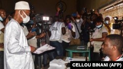 Le principal candidat de l'opposition Cellou Dalein Diallo reçoit son bulletin de vote d'un responsable de la commission électorale dans un bureau de vote à Conakry le 18 octobre 2020, lors des élections présidentielles en Guinée. (Photo par CELLOU BINANI / AFP)
