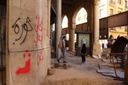 Many of the boards closing up this abandoned building have been torn down and graffiti, including writing that says "revolution" and "all of them means all of them," now covers the walls, in Beirut, Nov. 19, 2019. (Heather Murdock/VOA)