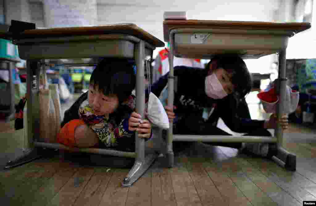Schoolchildren take shelter under desks during an earthquake simulation exercise in an annual drill at an elementary school in Tokyo, a day before the six-year anniversary of the 2011 earthquake and tsunami disaster that killed thousands and set off a nuclear crisis.